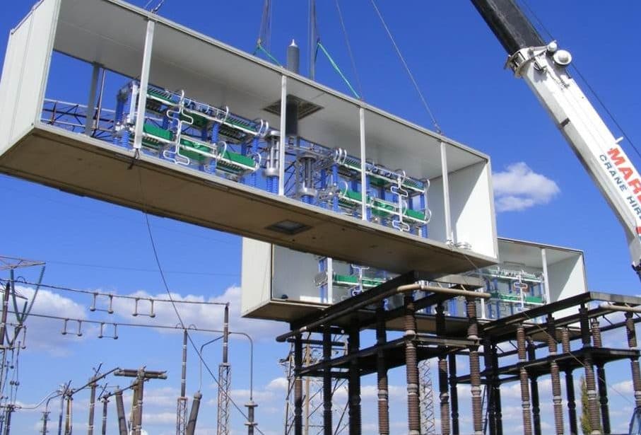 A capacitor bank platform being lifted into position by crane at a substation