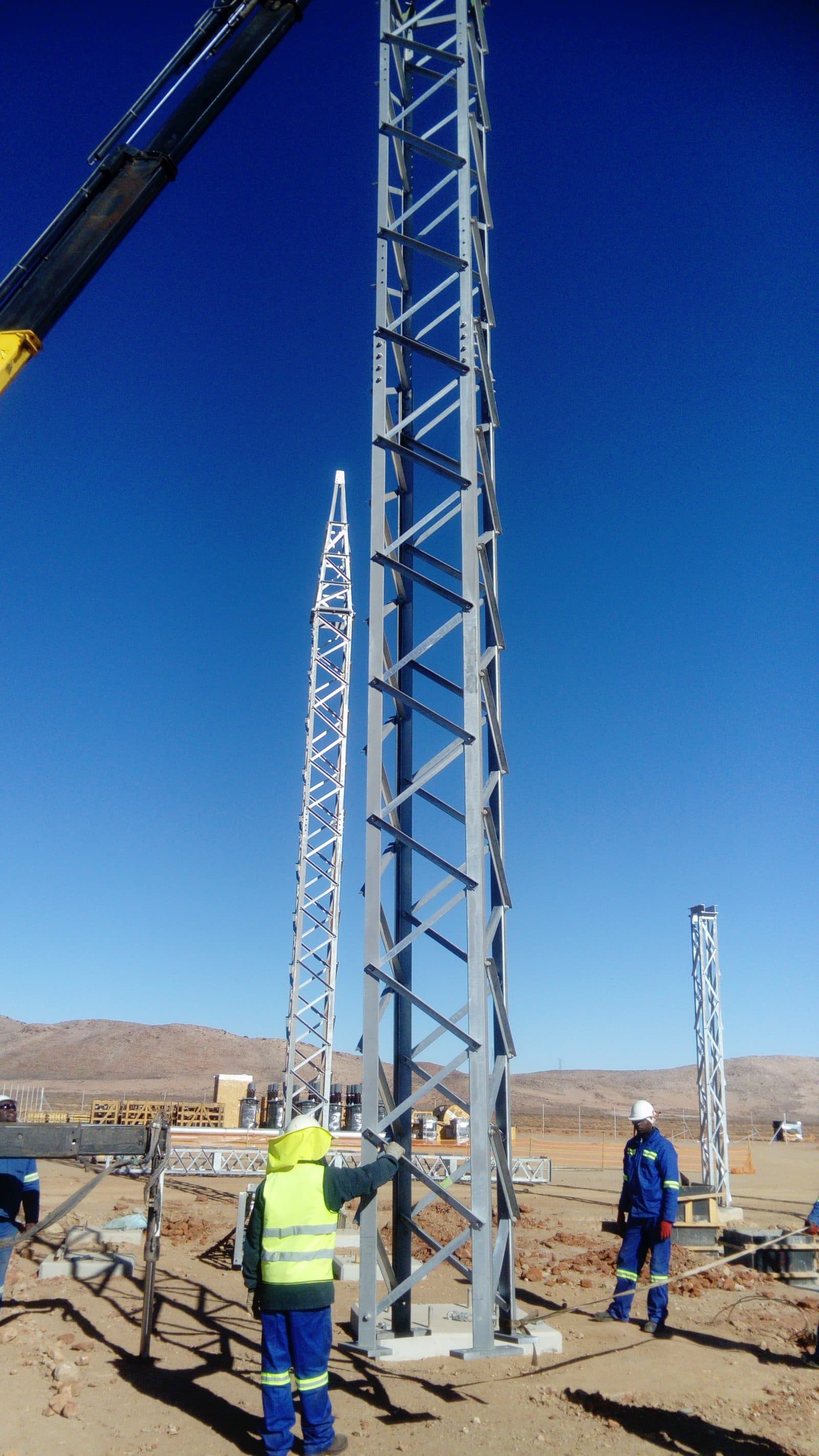 Site crew in high-visibility PPE bolting a lattice steel structure